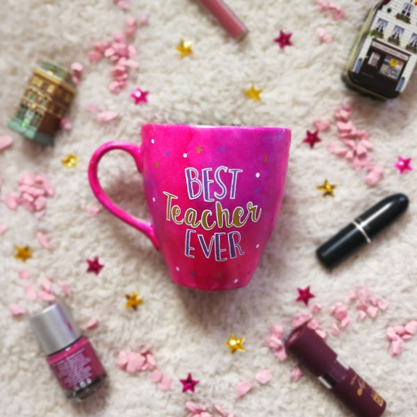 A indian pink hand painted mug with the words "Best teacher Ever" where Best and ever words are in purple and teacher is written in cursive in gold