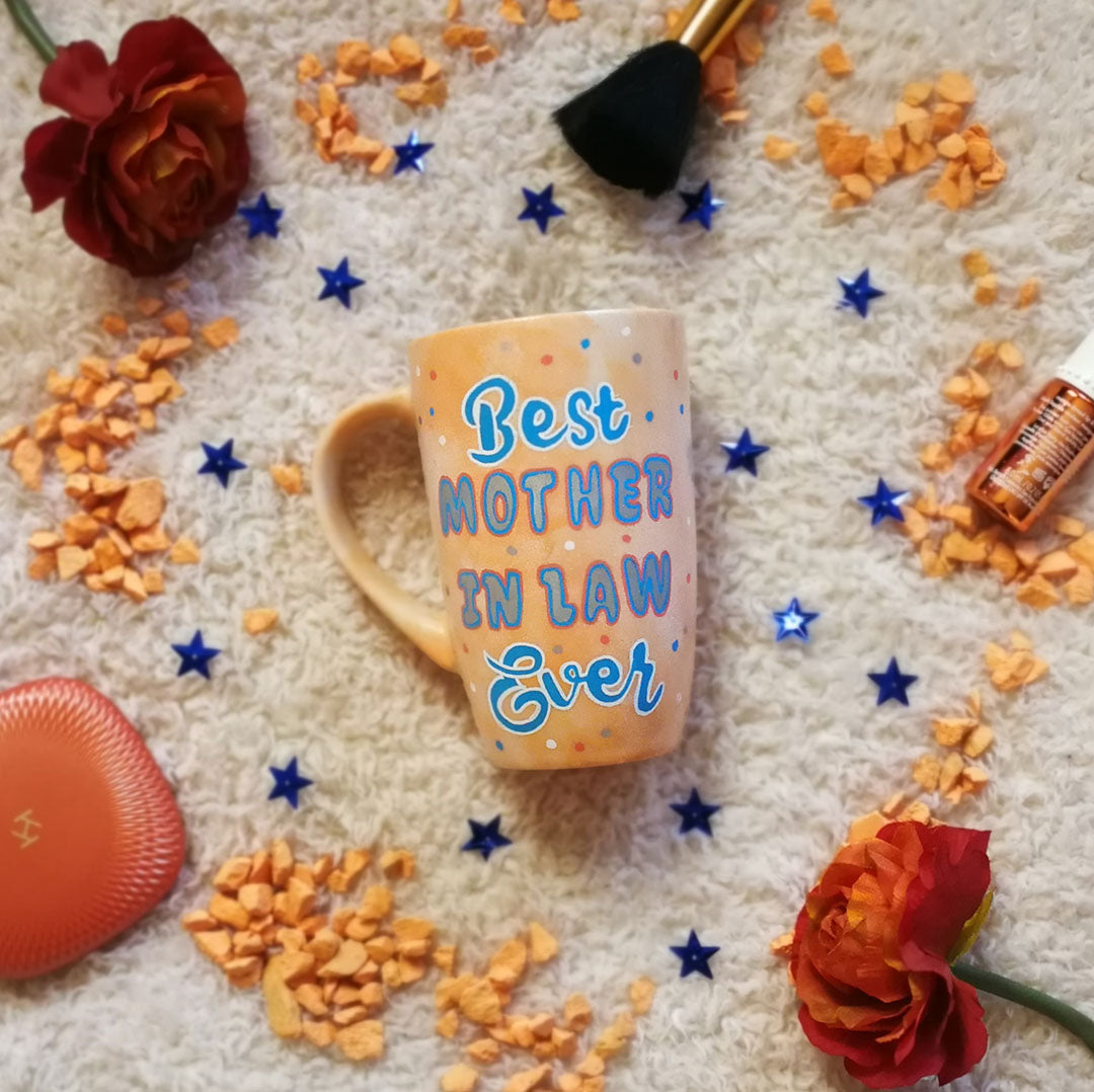 A baby orange mug with the words "Best Mother in Law Ever" with blue orange and white dots scattered all over