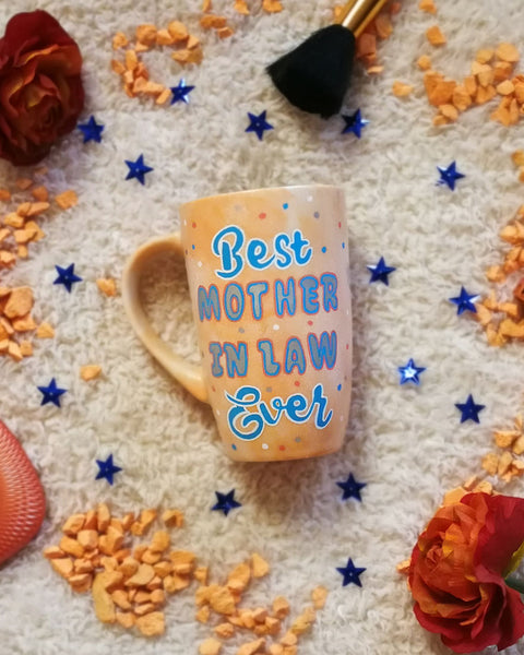 A baby orange mug with the words "Best Mother in Law Ever" with blue orange and white dots scattered all over