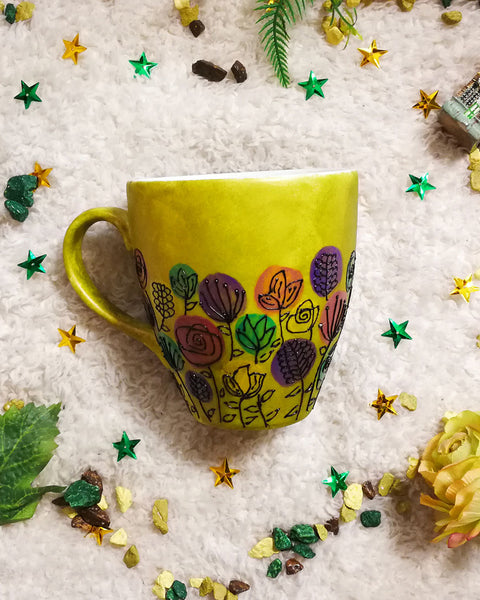 A Bronze hand painted mug with flowers drawn at the bottom half all around with black outliner and colored in purple, green,yellow and dark pink