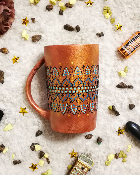 A Copper hand painted mug with patterns in the middle using black outliner and baby blue ,blue and gold dot art