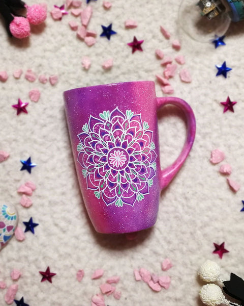 A Pink galaxy hand paitned mug with a mandala painted in the center with white