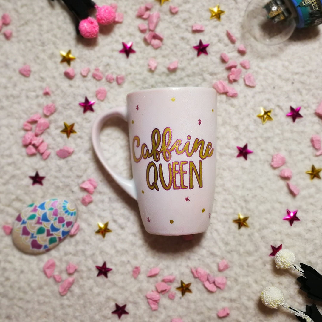 A Hand - painted baby pink mug with the words "Caffeine Queen" in gold