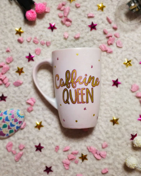 A Hand - painted baby pink mug with the words "Caffeine Queen" in gold