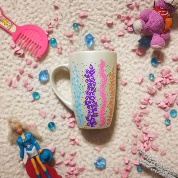 A pearl white hand painted mug with leaves draw on it vertically all over the mug from bottom to the top on colors of pink, green, blue, purple, orange and yellow