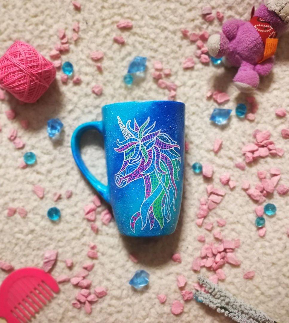 A blue galaxy hand painted mug with a zentangle unicorn design on it