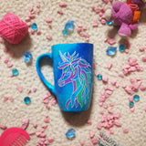 A blue galaxy hand painted mug with a zentangle unicorn design on it