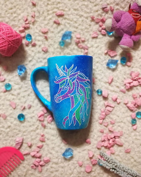 A blue galaxy hand painted mug with a zentangle unicorn design on it