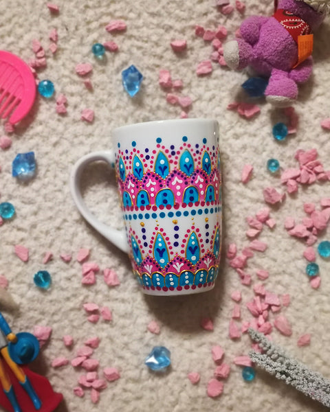 A White mug with patterns in pink and turquoise outlined with gold relief and dot art of white purple pink and turquoise.