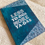 A Teal hand painted notebook witht he words "less to-dos more ta-das" written in the center and patterns on the top and bottom