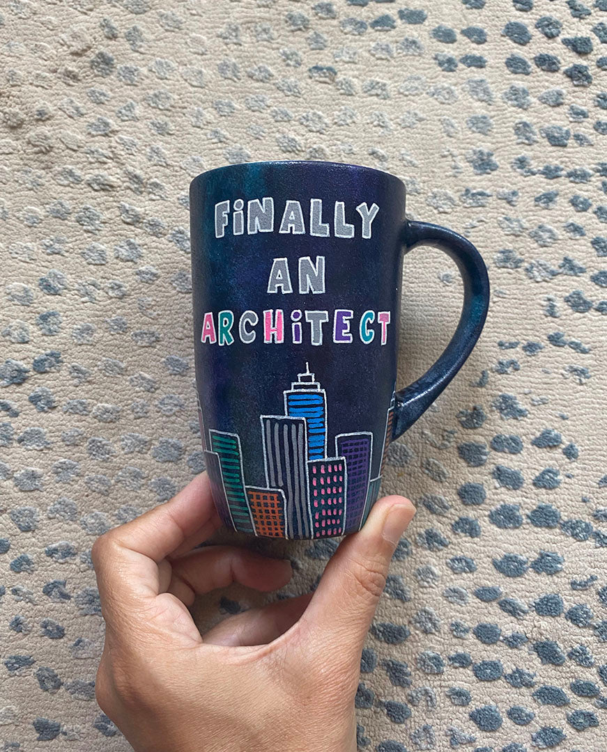 A Dark Sky handpainted mug with buildings drawn all over at the bottom half and the words "Finally and architect"