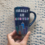 A Dark Sky handpainted mug with buildings drawn all over at the bottom half and the words 