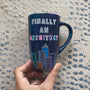 A Dark Sky handpainted mug with buildings drawn all over at the bottom half and the words "Finally and architect"