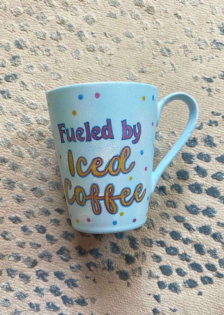 A baby blue hand painted mug with the words "fueled by iced coffee"