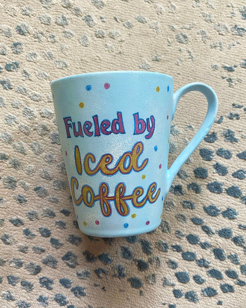 A baby blue hand painted mug with the words "fueled by iced coffee"