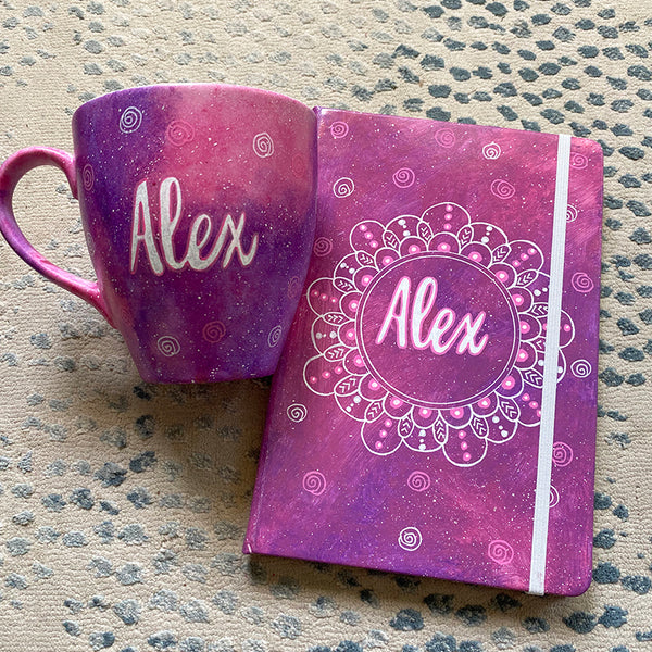 A Gift set of a mug and notebook in pink galaxy with the mug hacing the name alex and the notebook having the name alex in a mandala