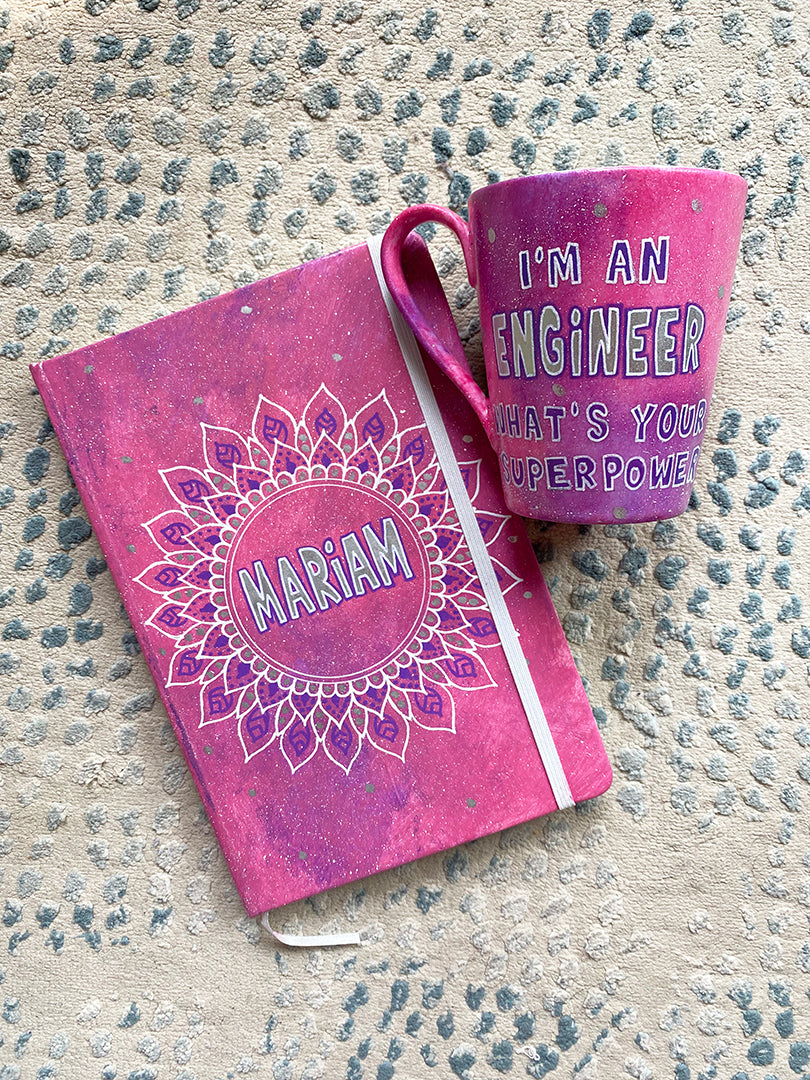 A Gift Set of mug and notebook in pink galaxy with the notebook having a mandala with the name mariam and the mug has the quote"Im an engineer what's your superpower"