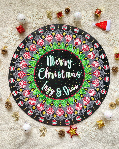 A Large 50cm in diameter mdf wooden plate, painted in black with a mandala drawn in white colored in green red and gold. and in the center the words "Merry christmas " written above and the names "Ingy and Diaa" written below