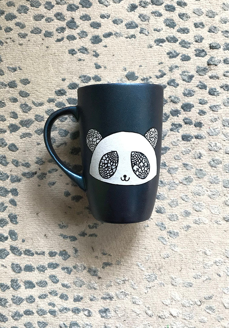 A Shimmery blue hand painted mug with a panda face in zentangles on it