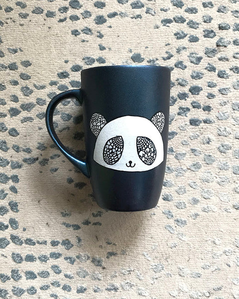 A Shimmery blue hand painted mug with a panda face in zentangles on it