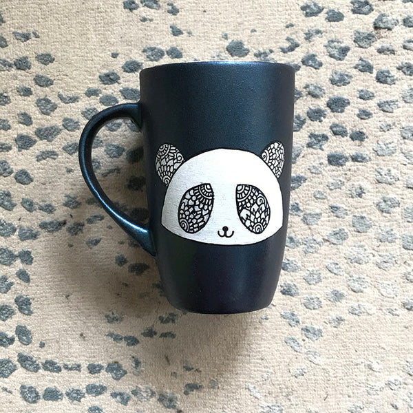 A Shimmery blue hand painted mug with a panda face in zentangles on it