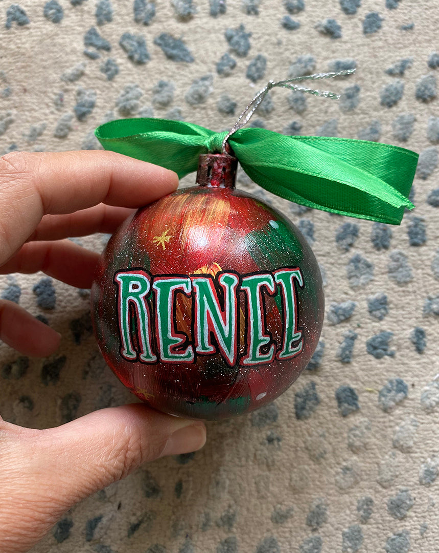 A Christmas galaxy hand painted ornament with the name "renee" written in green outlined with red and white and black