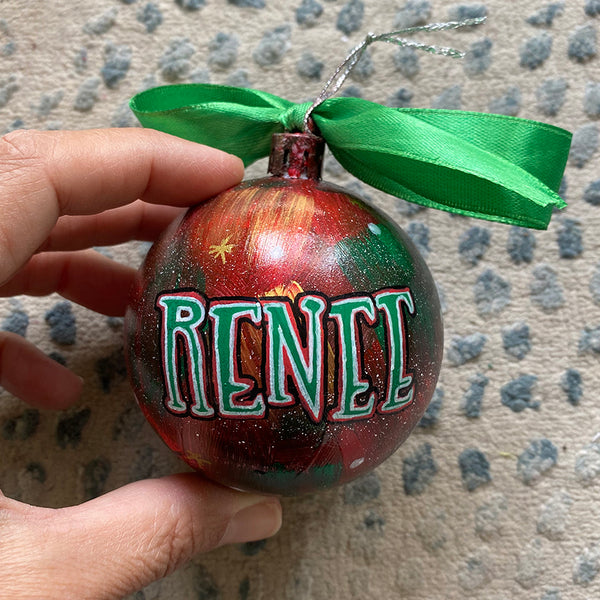 A Christmas galaxy hand painted ornament with the name "renee" written in green outlined with red and white and black