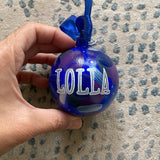 A Colorful hand painted ornament with ultramarine background and colors of ultramarine, dark purple, silver and grey scattered all over with white dots and the name 