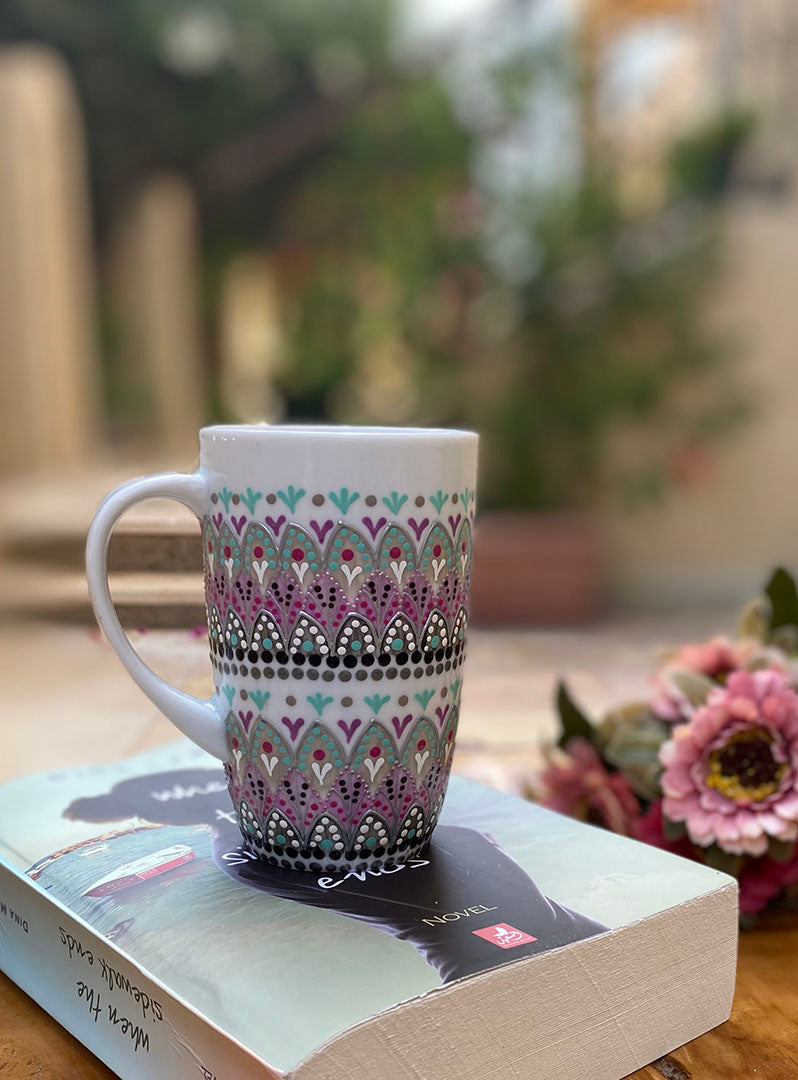 A white mug hand painted with patterns of taupe, grey and pastel pink, outlined with silver relief and dot art with mint green, black, pink, purple, grey and white