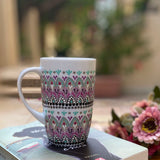 A white mug hand painted with patterns of taupe, grey and pastel pink, outlined with silver relief and dot art with mint green, black, pink, purple, grey and white