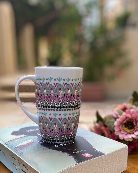 A white mug hand painted with patterns of taupe, grey and pastel pink, outlined with silver relief and dot art with mint green, black, pink, purple, grey and white