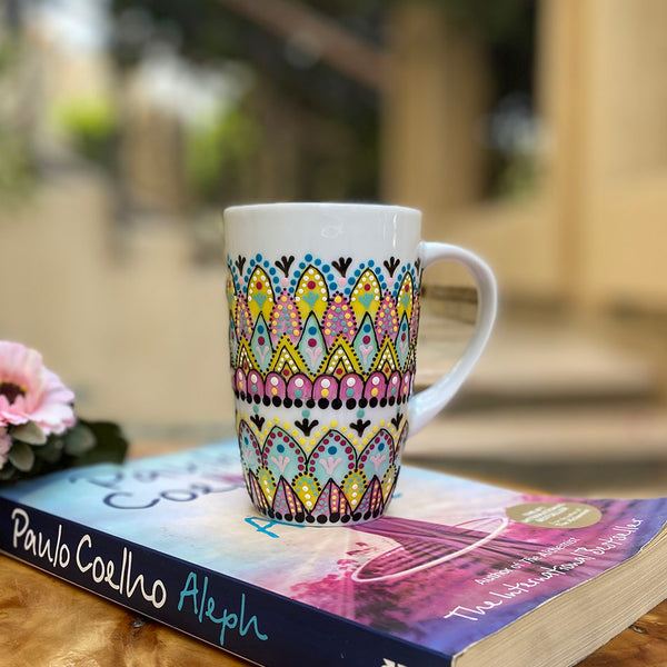 A white mug hand painted with patterns of yellow , pink and mint green , all outlined with black relief relief