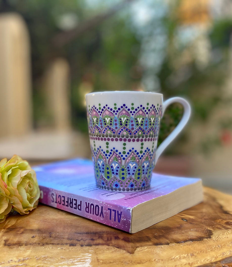 a white mug with patterns in lilac baby blue and pastel green outlined with silver relief and dot art of baby pink ultramarine blue, pastel green, lilac and white