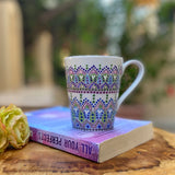 a white mug with patterns in lilac baby blue and pastel green outlined with silver relief and dot art of baby pink ultramarine blue, pastel green, lilac and white