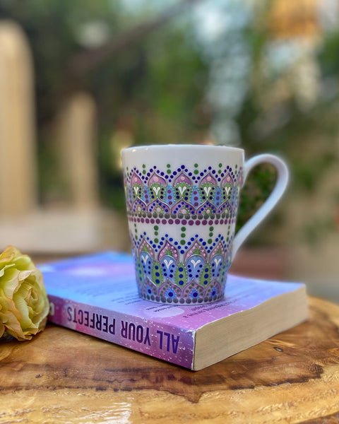 a white mug with patterns in lilac baby blue and pastel green outlined with silver relief and dot art of baby pink ultramarine blue, pastel green, lilac and white