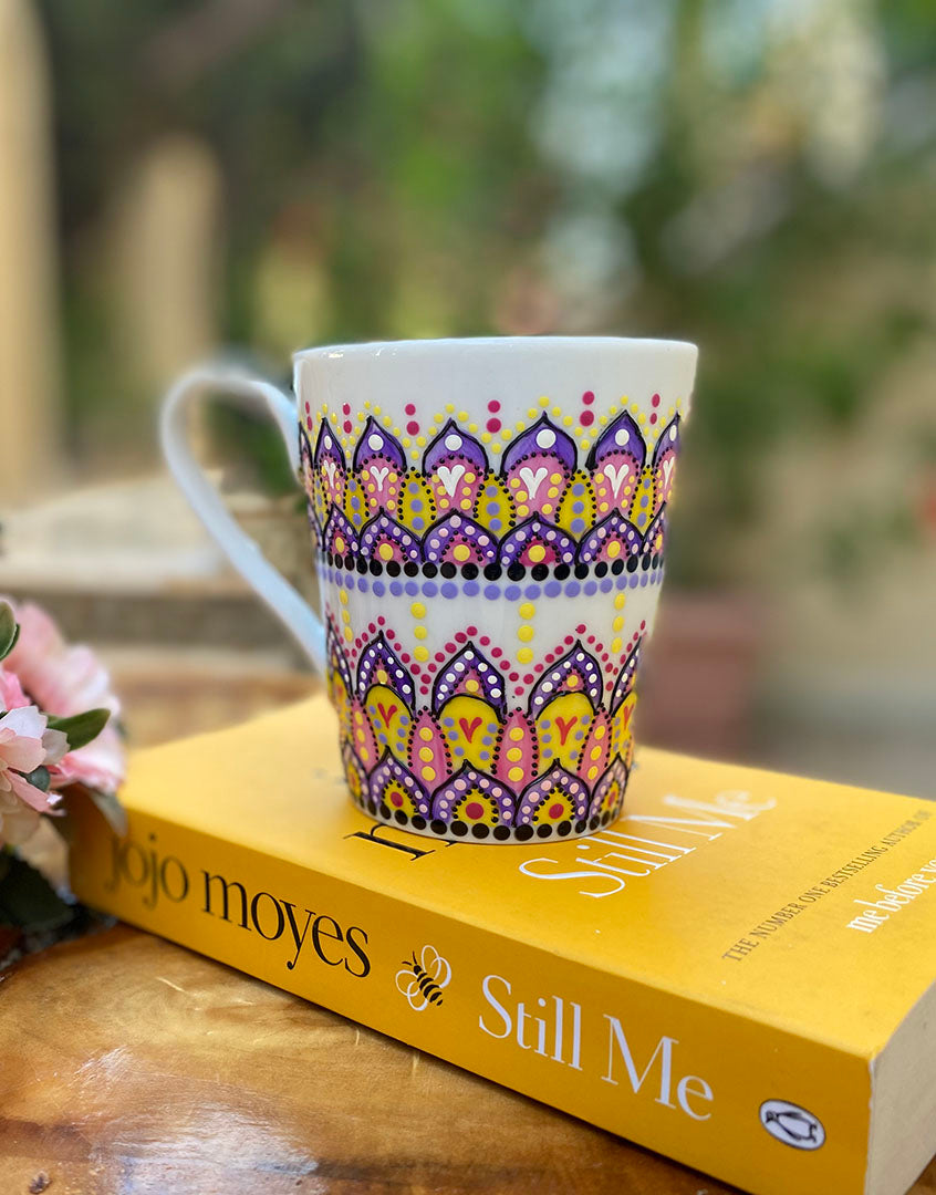 A white mug hand pa purple, yellow and pink outlined with black relief and dot art of purple , pink, yellow white and black