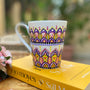 A white mug hand pa purple, yellow and pink outlined with black relief and dot art of purple , pink, yellow white and black