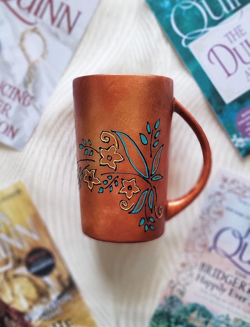 A Copper Hand Painted mug with relief drawings in black and glad of flowers and leaves on curved lines, with leaves colored in blue green