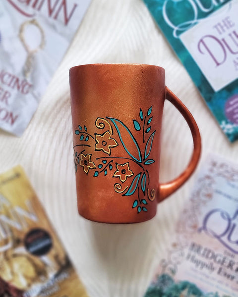 A Copper Hand Painted mug with relief drawings in black and glad of flowers and leaves on curved lines, with leaves colored in blue green