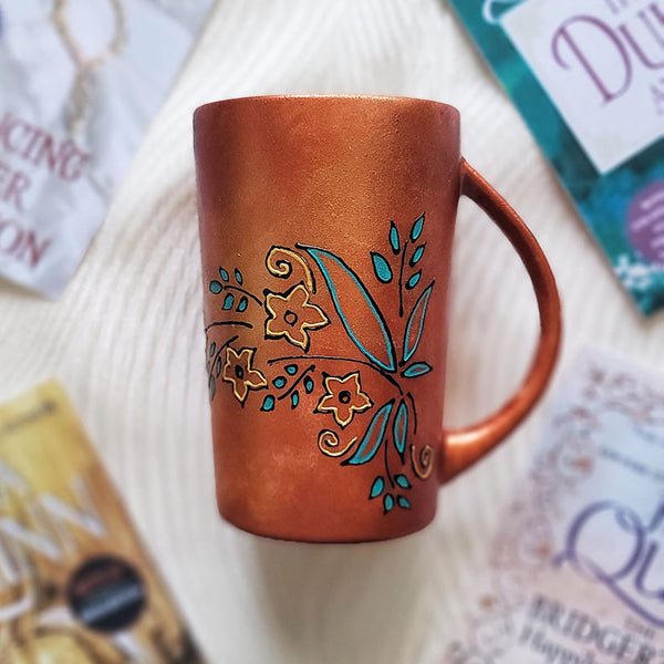 A Copper Hand Painted mug with relief drawings in black and glad of flowers and leaves on curved lines, with leaves colored in blue green