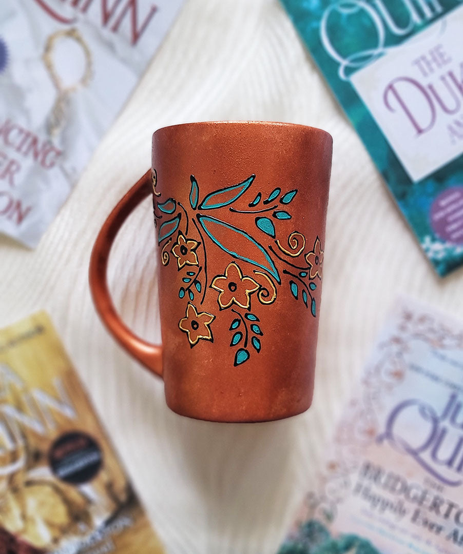 A Copper Hand Painted mug with relief drawings in black and glad of flowers and leaves on curved lines, with leaves colored in blue green