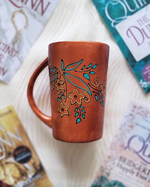 A Copper Hand Painted mug with relief drawings in black and glad of flowers and leaves on curved lines, with leaves colored in blue green