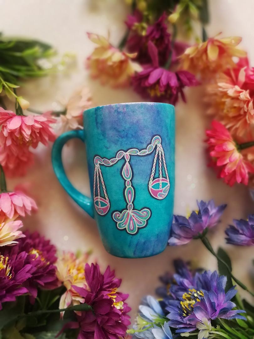 A Blue Galaxy hand painted mug with a libra design on it