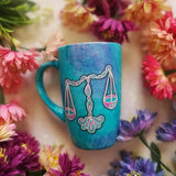 A Blue Galaxy hand painted mug with a libra design on it