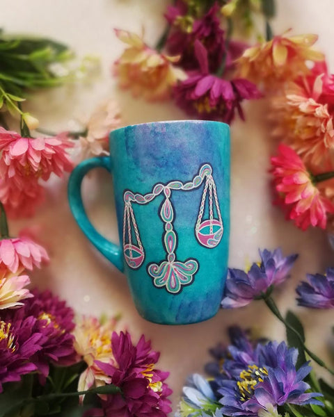 A Blue Galaxy hand painted mug with a libra design on it