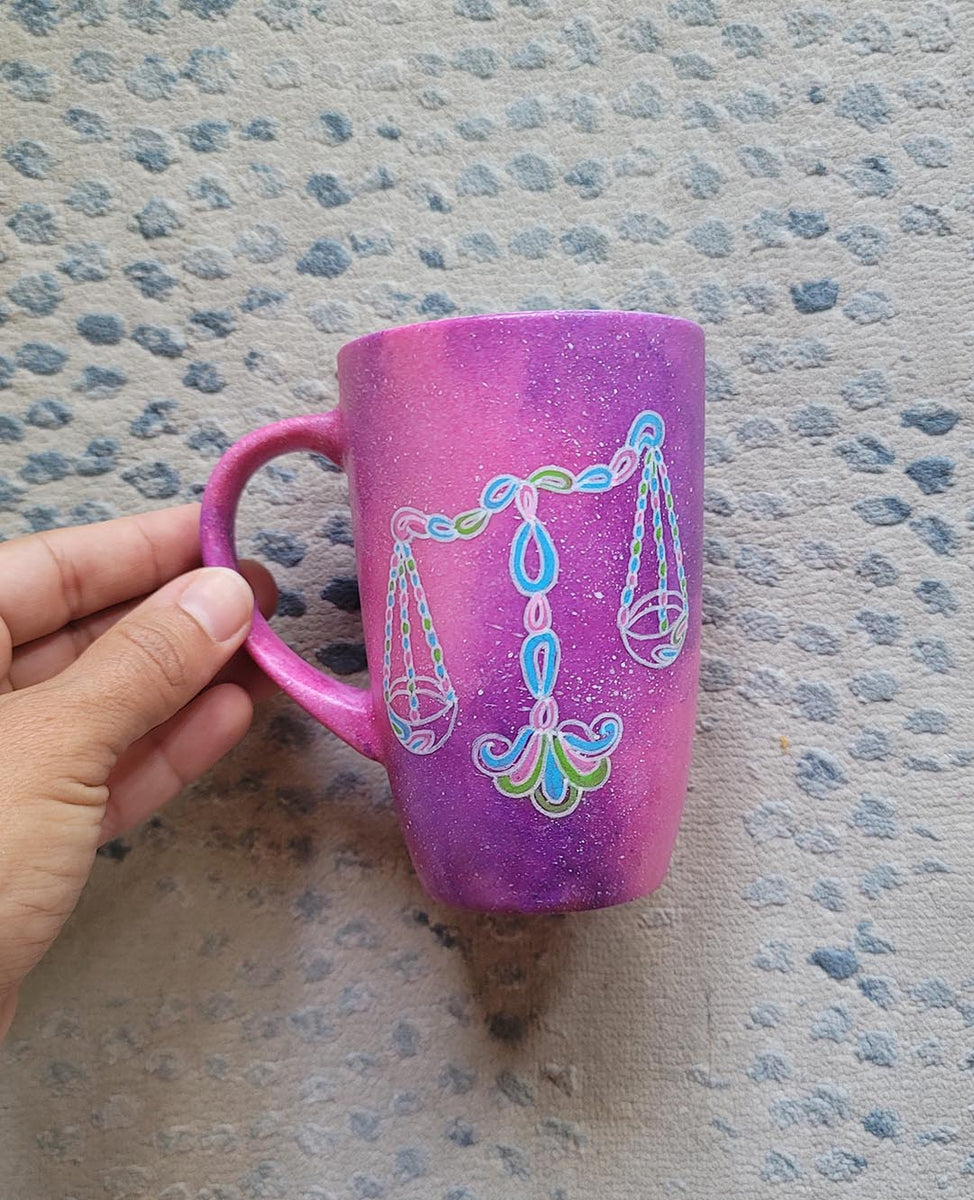 A Pink Galaxy hand painted mug with a libra design on it