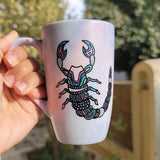 A Pale Hand painted Mug With a Scorpio Design on it in Black and colored in pinks, greens and blues