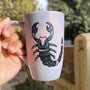 A Pale Hand painted Mug With a Scorpio Design on it in Black and colored in pinks, greens and blues