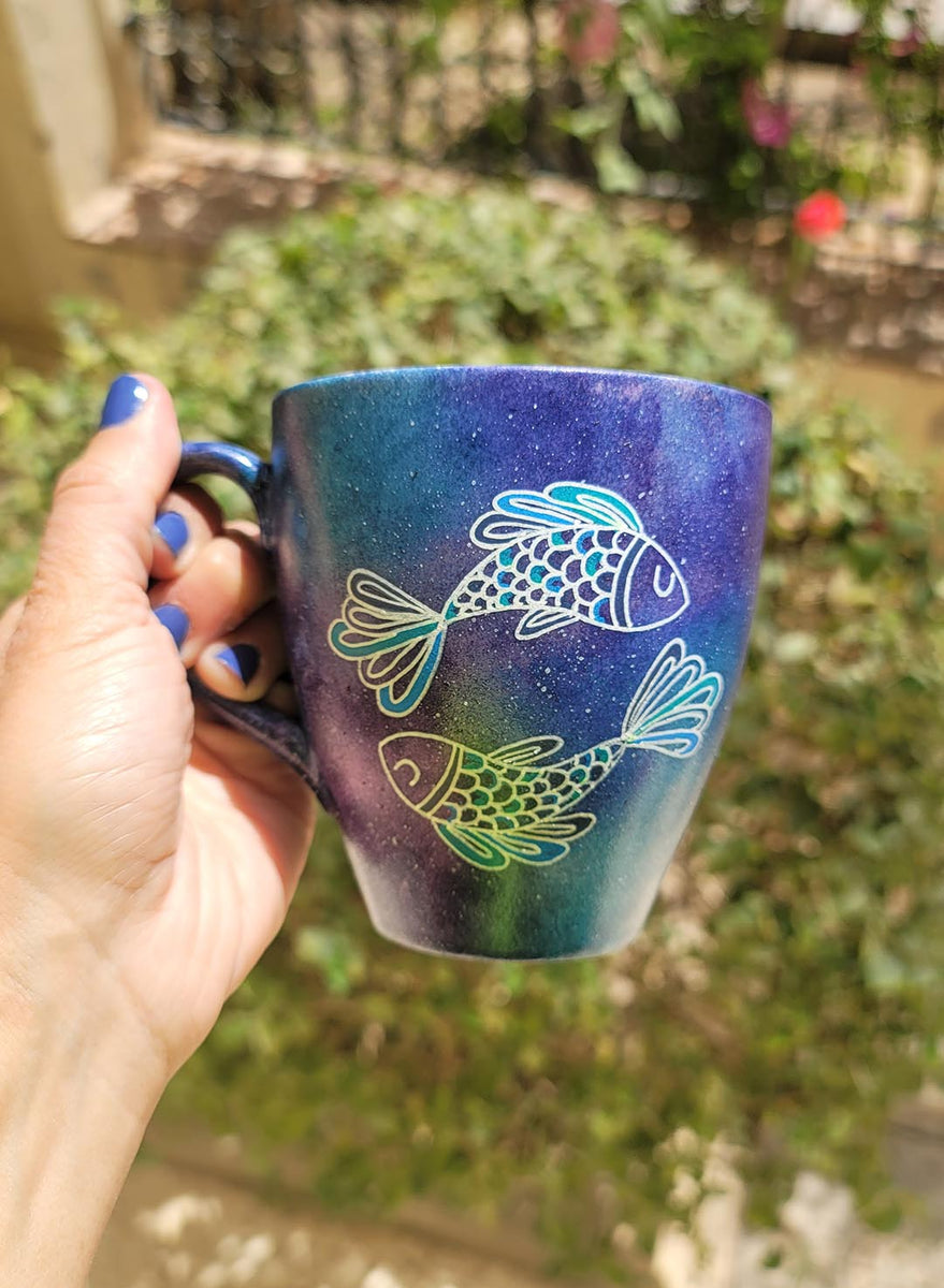 A Handpainted blue galaxy mug with a Pisces design on it