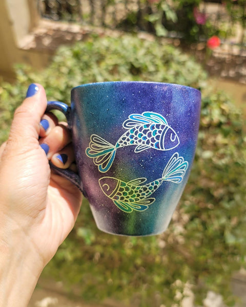 A Handpainted blue galaxy mug with a Pisces design on it